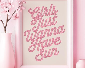 May include: A framed pink print with the words "Girls Just Wanna Have Sun" in a cursive font. The print is in a white frame, and there is a pink vase with flowers and petals in the foreground.