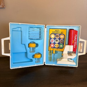 May include: A vintage Fisher-Price Micro Explorer Set in a white and blue plastic case. The set includes a microscope, specimen containers, and a booklet. The case is open, revealing the contents, with a red and white microscope.