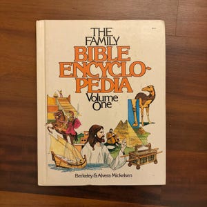 Könnte beinhalten: Ein Vintage-Hardcover-Buch mit dem Titel "THE FAMILY BIBLE ENCYCLOPEDIA Volume One". Das Cover zeigt Illustrationen biblischer Szenen, darunter ein Kamel, Pyramiden und Figuren in historischer Kleidung. Das Buch ist cremefarben mit orangefarbenen Buchstaben.