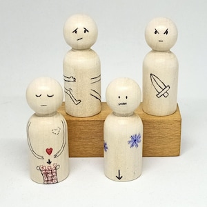 Könnte beinhalten: Vier Holz-Steckpuppen mit handbemalten Gesichtern und Details. Die Puppen stehen auf einem Holzblock. Eine Puppe hat ein Herz und einen Korb mit Herzen, eine andere ein Schwert, eine andere eine Schneeflocke und eine andere einen nach unten zeigenden Pfeil.