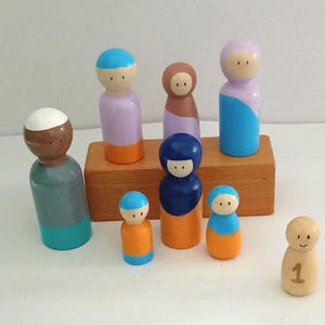 Peut inclure: Ensemble de poupées en bois peintes à la main, aux couleurs variées : bleu, orange, violet et marron. Certaines poupées sont disposées sur un petit bloc de bois. Une poupée porte le chiffre 1.