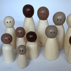 Op de afbeelding: Een set houten poppen met geverfde gezichten in verschillende bruintinten. De poppen zijn allemaal verschillend van grootte en hebben eenvoudige kenmerken.