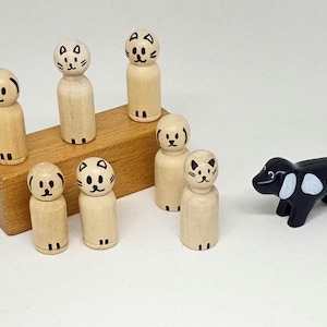 Op de afbeelding: Een set houten speelgoedkatten en -honden. Het speelgoed is zwart-wit geverfd en heeft eenvoudige gezichtskenmerken. Het speelgoed is gerangschikt op een houten blok.