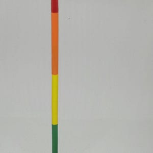 Pode incluir: Um bastão de madeira vermelho, laranja, amarelo e verde com uma bola vermelha no topo e uma base azul. Cinco prendedores de roupa de madeira estão na superfície branca abaixo do bastão.