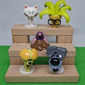 Op de afbeelding: Een verzameling kleurrijke beeldjes in cartoonstijl, waaronder een witte kat, een plant met een bril, een mol en twee honden. De beeldjes zijn gerangschikt op een kleine houten display, met een groene achtergrond.
