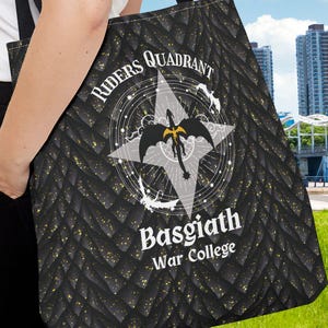 May include: Black tote bag with a repeating gold and black pattern. The bag features the text "Riders Quadrant" and "Basgiath War College" with a compass rose design. The bag has black straps and is carried over the shoulder.
