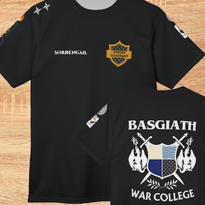 Könnte beinhalten: Schwarzes T-Shirt mit dem Text "SORRENGAIL" und einem gold-schwarzen Wappen mit der Aufschrift "RIDERS QUADRANT". Auf der Rückseite des Shirts steht "BASGIATH WAR COLLEGE" mit Wappen und gekreuzten Schwertern.