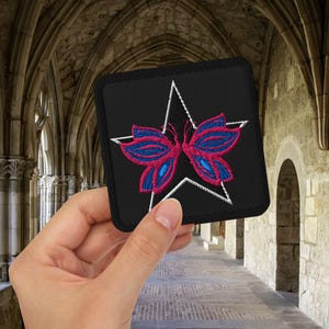 May include: A black square patch with a white star and a pink and blue butterfly embroidered on it.