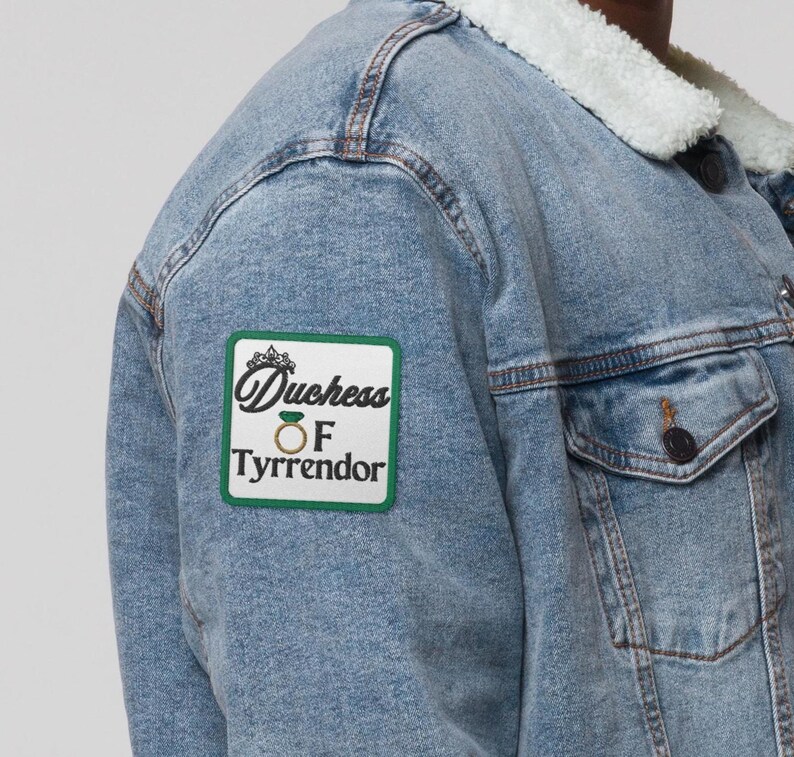 Pu&ograve; includere: Giacca di jeans blu chiaro con colletto in montone sintetico bianco. Una toppa verde e bianca sulla giacca recita "Duchess of Tyrrendor". La giacca ha due tasche frontali e bottoni scuri.