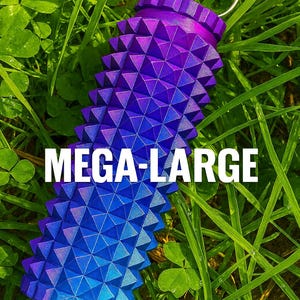 Op de afbeelding: Een object met een paarse en blauwe gradiënt met een gestructureerd, geometrisch ontwerp en een zilveren ring. De tekst "MEGA-LARGE" wordt in het wit weergegeven. Het object staat tegen een achtergrond van groen gras.