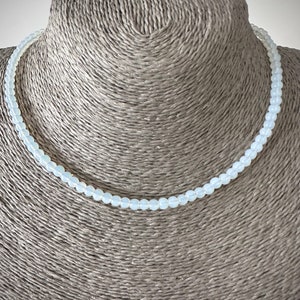 May include: A delicate white beaded necklace on a mannequin bust. The necklace is made of small, round beads that are strung together on a thin cord.