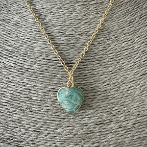 May include: A gold chain necklace with a green heart-shaped pendant. The pendant is made of a natural stone with a green and white marbled pattern.