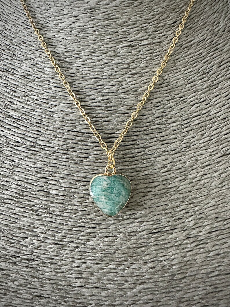 May include: A gold chain necklace with a green heart-shaped pendant. The pendant is made of a natural stone with a green and white marbled pattern.