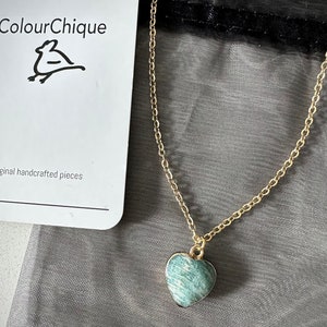 May include: A gold chain necklace with a green heart-shaped pendant. The pendant has a marbled pattern.