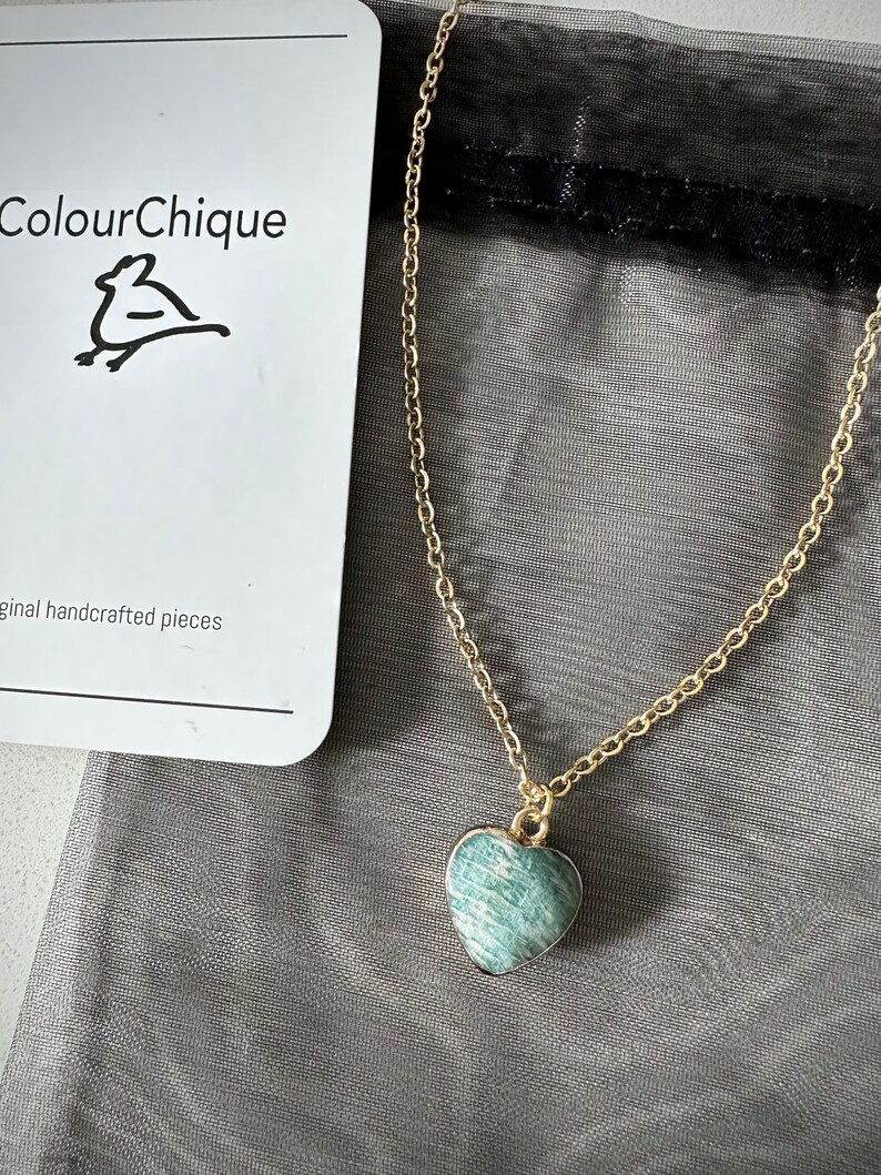 May include: A gold chain necklace with a green heart-shaped pendant. The pendant has a marbled pattern.