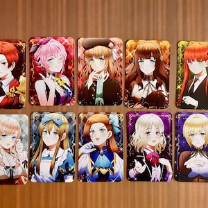 May include: A collection of ten rectangular trading cards featuring anime-style character illustrations. Each card displays a unique individual with distinct hair colors, outfits, and expressions, set against vibrant, decorative backgrounds with sparkles.