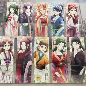 May include: A clear acrylic display case filled with colorful anime-style bookmarks. Each bookmark features a different character in traditional Asian clothing. The characters have various hair colors and are in different poses.