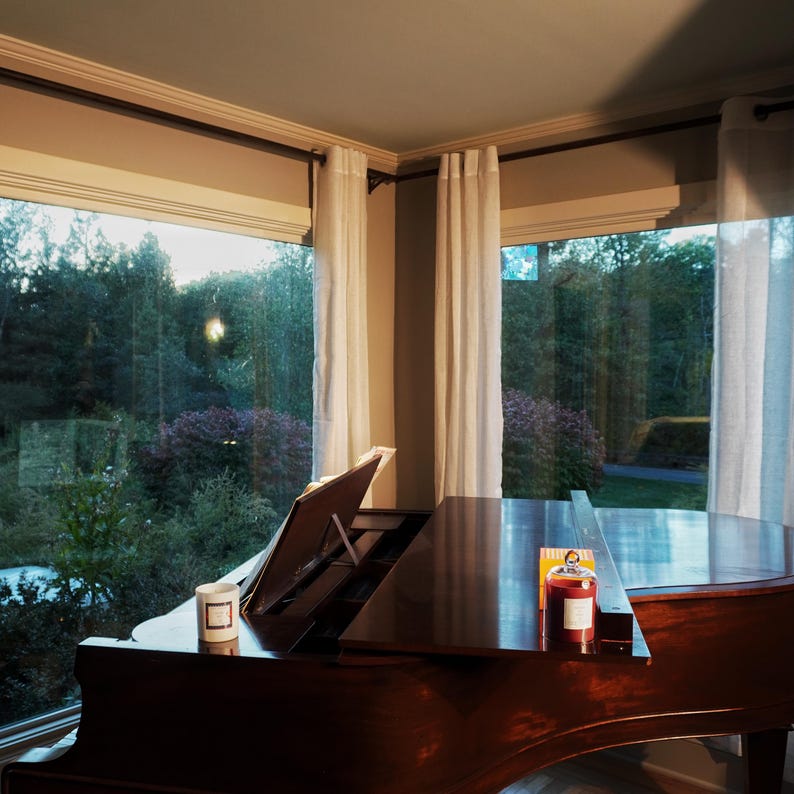 Aesthetic sunlit living room featuring a grand piano and a KEA ATELIER decorative glass jar candle by the window.