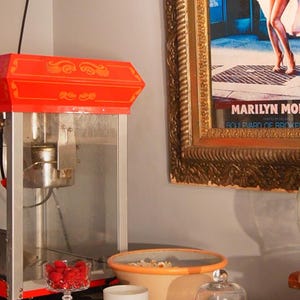 Vintage movie room aesthetic with a retro popcorn maker, Marilyn Monroe poster, and a KEA ATELIER soy wax candle on the table.