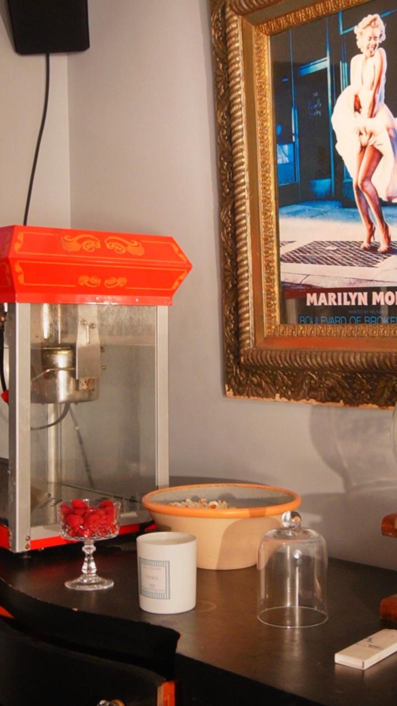Vintage movie room aesthetic with a retro popcorn maker, Marilyn Monroe poster, and a KEA ATELIER soy wax candle on the table.