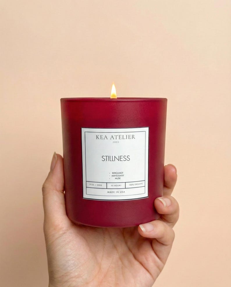 A hand elegantly holding a KEA ATELIER bold red glass jar soy candle, representing a luxurious masculine home decor gift.