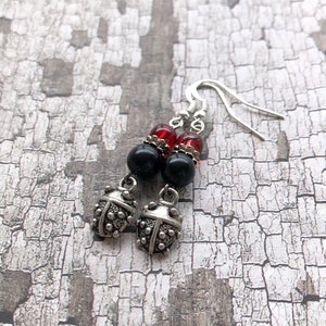 May include: Silver ladybug earrings with black and red beads. The earrings are dangling and have a silver hook.