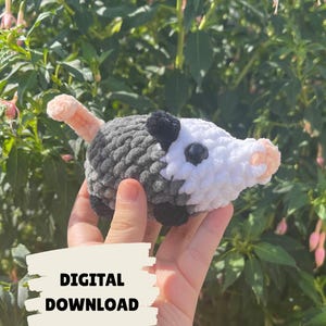 May include: A handmade crochet opossum toy in shades of gray, white, black, and peach. The plush animal has a rounded body, small black eyes, and a pink nose and tail. The text "DIGITAL DOWNLOAD" is on a beige rectangle.