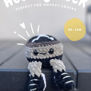 May include: A crocheted hockey puck plushie with black and grey yarn, featuring black safety eyes, a small smile, and two dangling legs wearing black and white skates. The image includes text reading Hockey Puck, no-sew, and DIGITAL PDF DOWNLOAD.