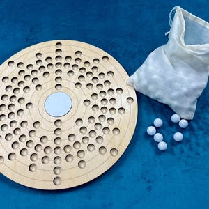 May include: A wooden game board with a circular design and a white center circle. The board has many small holes around the center circle. A white cloth bag and white marbles are also included.