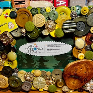 May include: A green picture frame decorated with colorful buttons, including yellow, green, brown, and white. The frame is surrounded by a variety of buttons, including some with a floral design. The frame is titled "All Buttoned Up By Tina" and includes the text "Unique Button Creations" and "Each design, one of a kind".