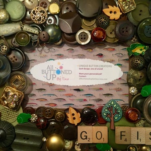 May include: A framed artwork made of buttons, beads, and other small objects. The artwork features a fish theme with the words "Go Fish" spelled out in Scrabble tiles. The frame is surrounded by a variety of buttons in different colors and textures. A business card for "All Buttoned Up By Tina" is visible in the center of the frame.