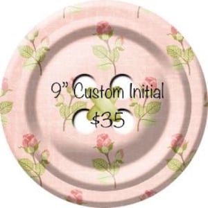 May include: A 9" custom initial button with a pink floral pattern. The button has three holes and the text "$35" is printed on it.