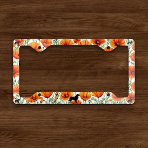 May include: Rectangular license plate frame featuring a floral design with orange poppies and green leaves on a white background. Black silhouettes of a dog are interspersed throughout the design. The frame is made of a durable material.