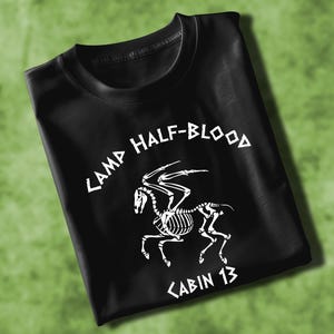 Może przedstawiać: Czarny T-shirt z białym nadrukiem szkieletu skrzydlatego konia i tekstem "Camp Half-Blood Cabin 13".