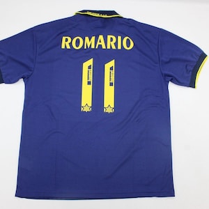 Puede incluir: Camiseta de fútbol azul marino con el nombre "ROMARIO" y el número "11" en amarillo. La camiseta tiene cuello amarillo y ribete amarillo en las mangas. El número "11" se muestra dos veces en la parte posterior.