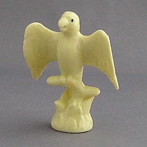 May include: A small, white ceramic figurine of a parrot perched on a branch. The parrot has its wings spread out and its head tilted to the side.