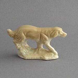 May include: A small, cream-coloured ceramic figurine of a dog running. The dog is in a realistic pose with its head turned to the side and its tail wagging.