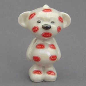 May include: White ceramic teddy bear figurine with red polka dots. The bear has a black nose and black eyes.