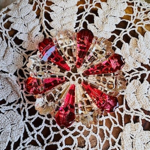 May include: A circular glass dish featuring a radial pattern of alternating clear and deep red segments. The dish has a scalloped edge and a faceted design that creates a star-like appearance, with a hollow center and a smooth, reflective surface.