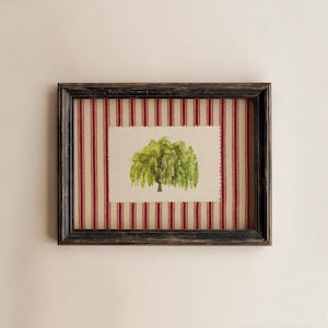 May include: A framed watercolor painting of a weeping willow tree. The artwork is set against a red and white striped background, enclosed in a distressed black wooden frame. The tree features green foliage and a brown trunk.