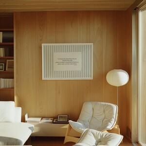 May include: A light-filled interior with wood-paneled walls and a framed artwork. The artwork features a striped background and text. A white sofa, chair, and floor lamp are also visible, creating a minimalist and serene atmosphere.