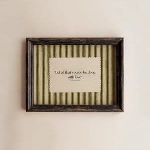 May include: A framed print with the quote "Let all that you do be done with love." The frame is dark brown with a distressed finish. The background features vertical green and white stripes.