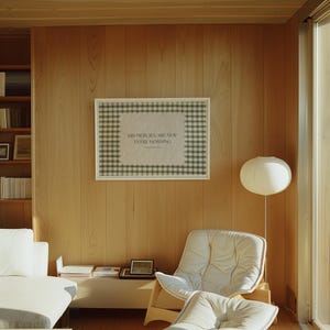 May include: A framed print with the text "HIS MERCIES ARE NEW EVERY MORNING" against a checkered background hangs on a wood-panelled wall. The room features a white sofa, a chair, and a floor lamp with a round shade, creating a minimalist aesthetic.