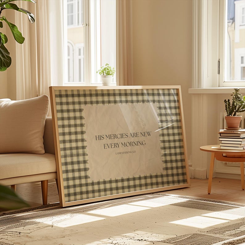 May include: A framed print with a light wood frame. The print features a gingham pattern in shades of grey and white, surrounding a central text that reads "HIS MERCIES ARE NEW EVERY MORNING". The artwork is displayed in a well-lit living room setting.