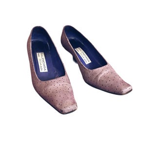 May include: A pair of light brown, square-toe pumps with small, dark dots. The shoes have a low heel and a purple interior. The brand name "BALENCIAGA PARIS El Corte Ingles" is printed inside each shoe.