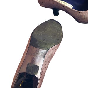 May include: Two light brown Balenciaga pumps with small black heels. The shoes have a perforated pattern and a pointed toe. The sole of one shoe is visible, showing the size 37 and the Balenciaga brand.