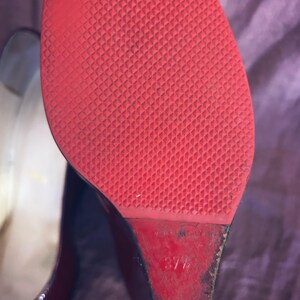 May include: Close-up of the sole of a red high-heeled shoe. The sole has a textured pattern. The heel is a wedge shape. The size is marked as 37 1/2. The shoe is made in Italy.
