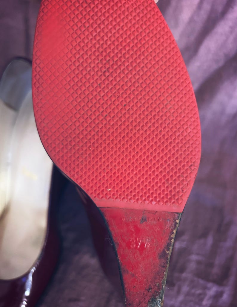May include: Close-up of the sole of a red high-heeled shoe. The sole has a textured pattern. The heel is a wedge shape. The size is marked as 37 1/2. The shoe is made in Italy.