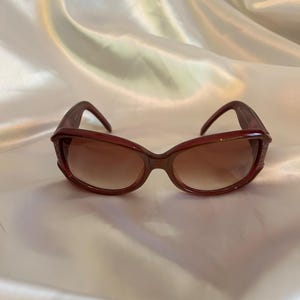 Puede incluir: Gafas de sol tintadas en marrón con montura marrón oscuro. Las gafas de sol tienen forma redondeada y están sobre un fondo blanco. Las lentes tienen un tinte degradado, que pasa de un tono más oscuro en la parte superior a un tono más claro en la parte inferior.