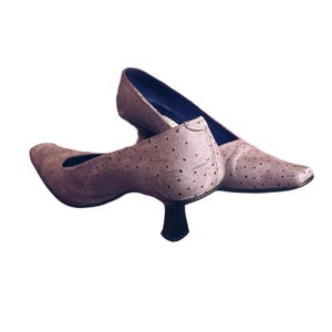May include: A pair of light purple pumps with a pointed toe and a small, black heel. The shoes have a textured surface with small, evenly spaced dots. The interior of the shoe is a dark blue color.